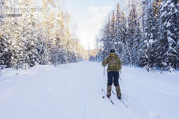 Rückansicht eines Mannes mit Rucksack beim Skifahren auf schneebedecktem Feld