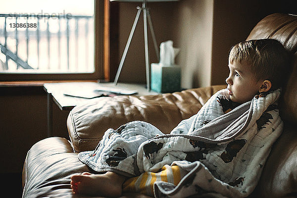 Nachdenklicher  in eine Decke gehüllter Junge  der sich zu Hause auf dem Sofa entspannt