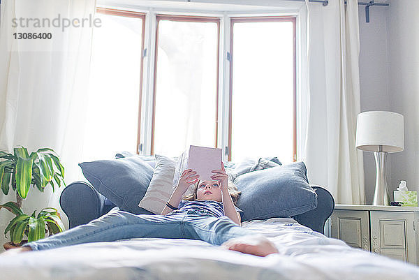 Mädchen liest Buch  während sie zu Hause auf dem Bett liegt