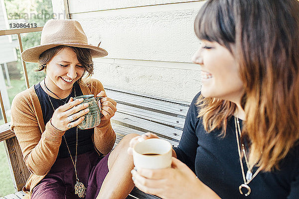 Lächelnde Freundinnen trinken Kaffee  während sie auf einer Holzbank sitzen