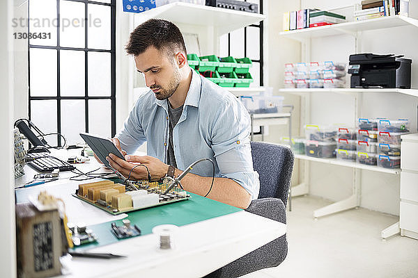 Seriöser Ingenieur  der einen Tablet-Computer benutzt  während er am Tisch in der Elektronikindustrie arbeitet