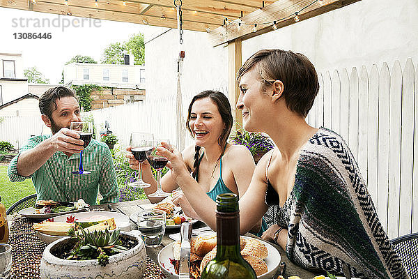 Freunde stoßen auf Weingläser an  während sie am Tisch im Hof sitzen