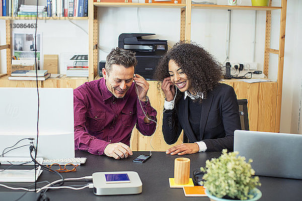 Glückliche Kollegen mit Mobiltelefon am Tisch im Büro