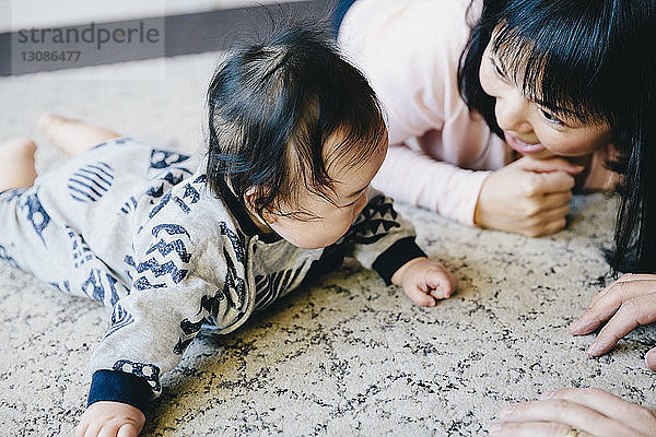 Schrägaufnahme einer glücklichen Mutter  die mit ihrem Sohn spielt  während sie zu Hause auf dem Teppich liegt