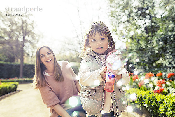 Glückliche Frau mit Tochter hält Blasenpistole im Park