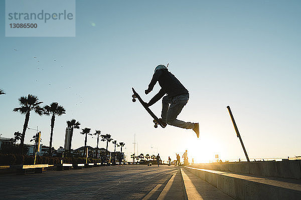 Seitenansicht eines Mannes  der einen Stunt beim Skateboardfahren auf der Straße gegen den Himmel ausführt