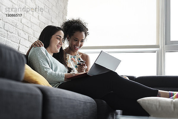 Niedriger Blickwinkel auf ein glückliches lesbisches Paar beim Online-Shopping  während es zu Hause auf dem Sofa sitzt