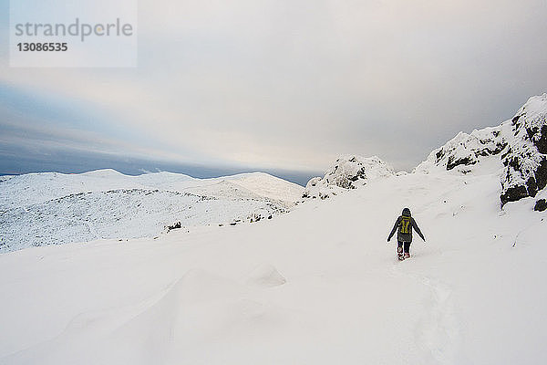 Rückansicht eines Wanderers  der auf einem schneebedeckten Berg vor bewölktem Himmel wandert