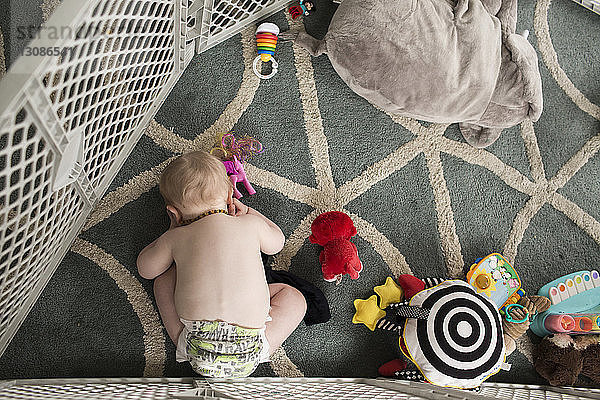 Hochwinkelaufnahme eines Jungen ohne Hemd  der mit Spielzeug spielt  während er sich zu Hause auf dem Teppich bückt