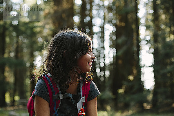 Glückliches Mädchen mit Rucksack schaut weg  während sie im Wald sitzt