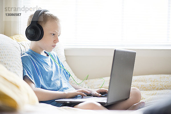 Junge hört Musik  während er zu Hause einen Laptop benutzt