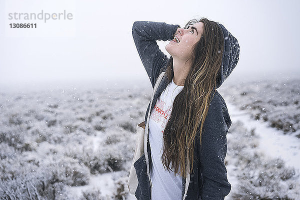 Frau mit langen Haaren schaut nach oben  während sie auf schneebedecktem Feld steht
