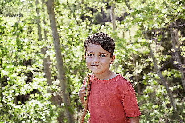Porträt eines süßen Jungen mit Stock in der Hand im Wald