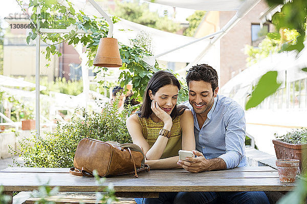 Paare  die zusammen ein Smartphone benutzen  im Straßencafé