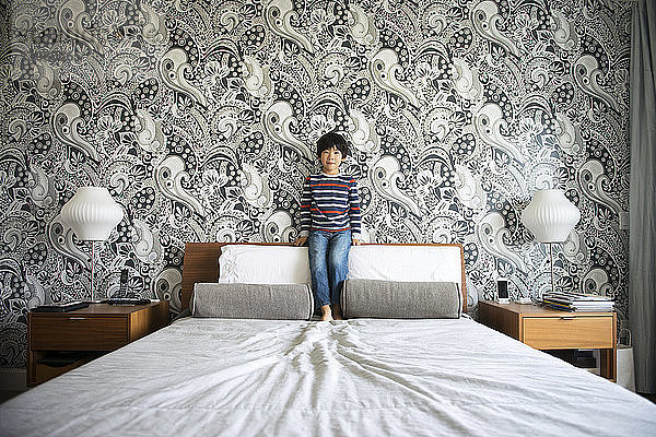 Junge steht auf Bett gegen Wand im Schlafzimmer