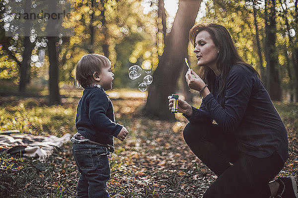Mutter und Sohn spielen im Herbst im Park mit Seifenblasen