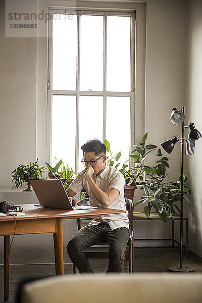 Geschäftsmann mit Laptop  während er im Kreativbüro am Tisch gegen das Fenster sitzt
