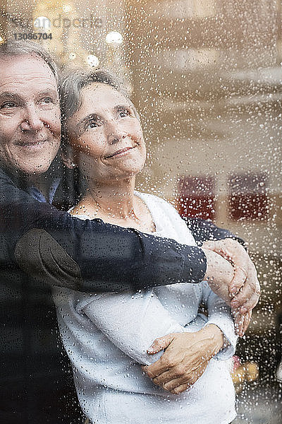 Liebevolles älteres Paar schaut durch nasses Fenster