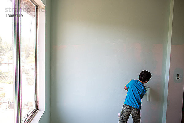 Rückansicht eines Jungen  der zu Hause eine Wand mit einem Farbroller bemalt