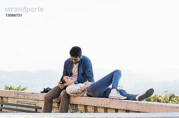 Romantisches Paar entspannt sich auf einer Stützmauer auf einer Terrasse bei klarem Himmel