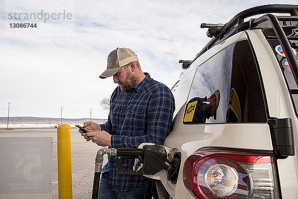 Mittelgroßer erwachsener Mann  der ein Smartphone benutzt  während er an der Tankstelle im Auto steht