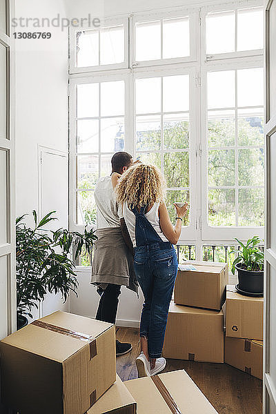 Rückansicht eines Paares  das durch ein Fenster schaut  während es in seinem neuen Zuhause steht  durch eine Tür