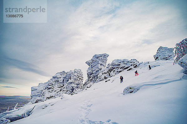 Wanderer erklimmen schneebedeckte Berge gegen wolkigen Himmel