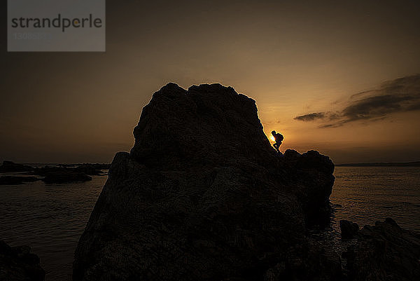 Silhouette Kind klettert am Fels am Strand gegen den Himmel bei Sonnenuntergang