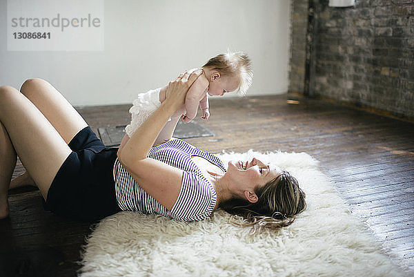 Hochwinkelaufnahme einer Mutter  die ihre Tochter hebt  während sie zu Hause auf einem pelzigen Teppich liegt
