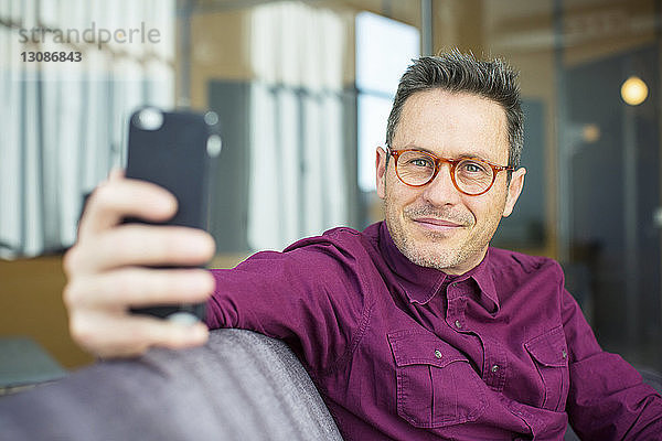 Porträt eines Geschäftsmannes  der ein Mobiltelefon benutzt  während er im Büro auf dem Sofa sitzt