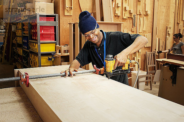 Fröhlicher Zimmermann bohrt Holzbohlen in der Werkstatt