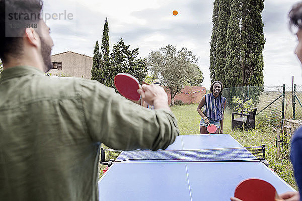 Multi-ethnische Freunde spielen Tischtennis im Hof