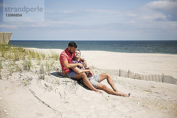 Homosexuelles Paar ruht sich am Strand gegen den Himmel