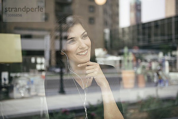 Glückliche Frau  die Musik hört  während sie durch ein Fenster im Café durch Glas gesehen wird