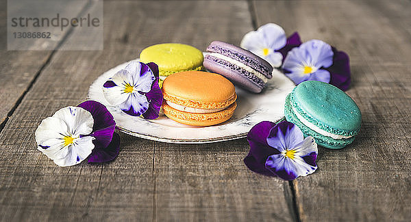 Hochwinkelansicht von bunten Makronen mit Blumen auf Holztisch