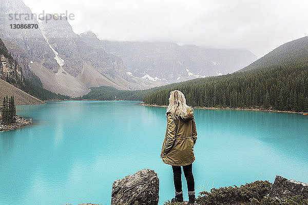 Rückansicht einer Wanderin mit der Hand in der Tasche  die am Moraine Lake vor den Bergen im Banff-Nationalpark steht