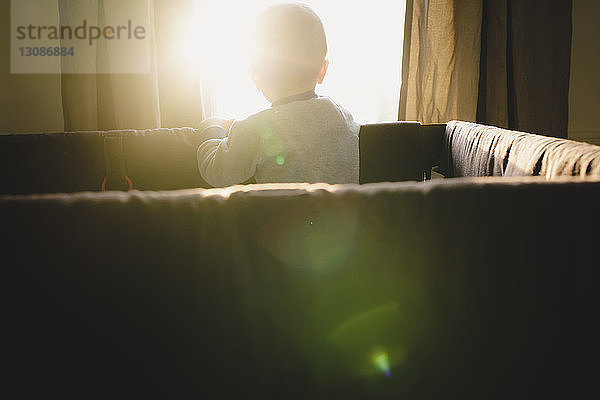 Rückansicht eines kleinen Jungen im Kinderbett zu Hause am Fenster