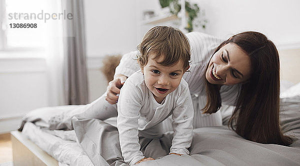 Porträt eines verspielten kleinen Jungen mit der Mutter zu Hause im Bett