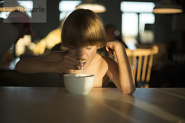 Junge ohne Hemd frühstückt am Tisch