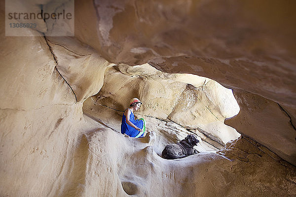 Niedrigwinkelansicht eines auf einem Felsen sitzenden Mädchens und Hundes