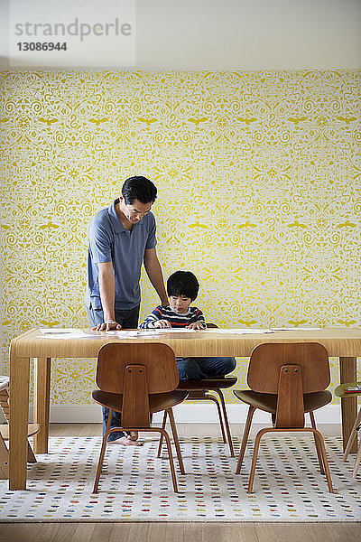 Vater hilft dem Jungen zu Hause bei den Hausaufgaben an der Wand