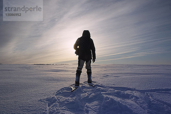 Rückansicht eines Mannes  der an einem sonnigen Tag auf einem schneebedeckten Feld gegen den Himmel steht