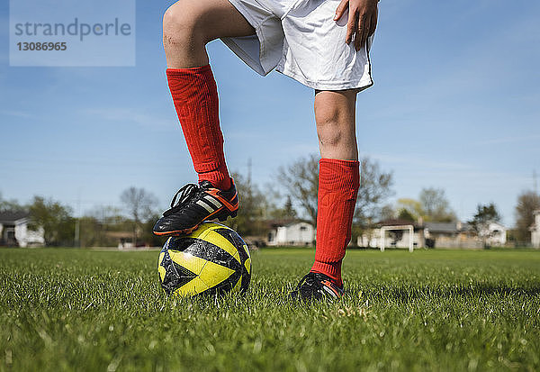 Niedriger Teil eines Jungen mit Fussball  der auf Grasfeld gegen den Himmel steht