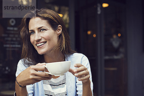 Glückliche Frau schaut weg  während sie im Straßencafé eine Kaffeetasse hält
