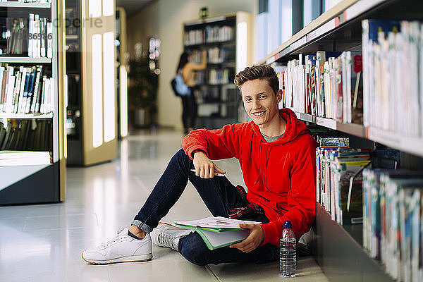 Porträt eines Mannes  der in der Bibliothek auf dem Boden sitzend studiert