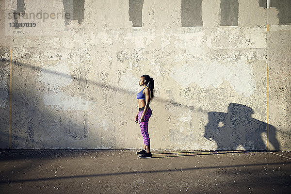Seitenansicht einer Sportlerin  die auf der Strasse an der Wand steht