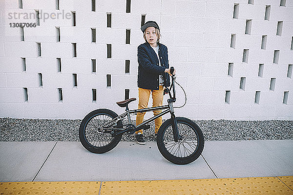 Porträt eines Jungen mit Fahrrad in voller Länge  der in der Stadt an der Wand steht