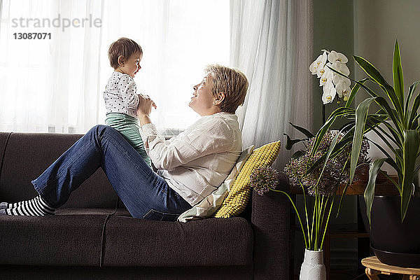 Seitenansicht einer glücklichen Frau  die mit ihrer Enkelin auf dem Sofa am Fenster spielt