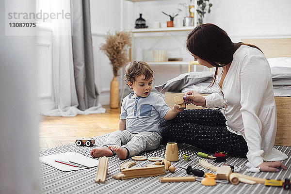 Mutter und kleiner Junge stoßen zu Hause auf Spielzeug-Teetassen an  während sie auf dem Teppich sitzen