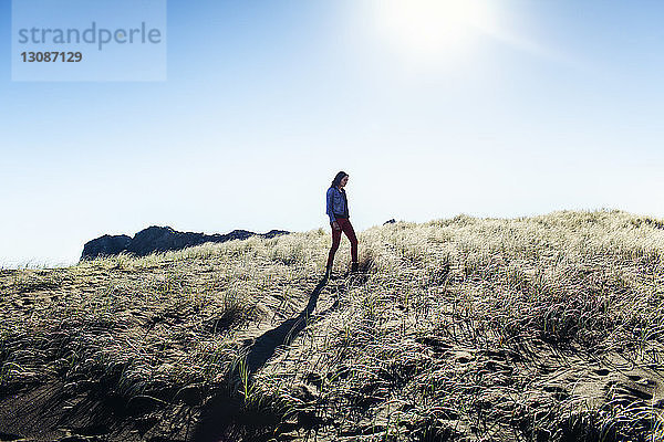 Seitenansicht einer Frau  die an einem sonnigen Tag auf einem Grasfeld vor klarem Himmel geht
